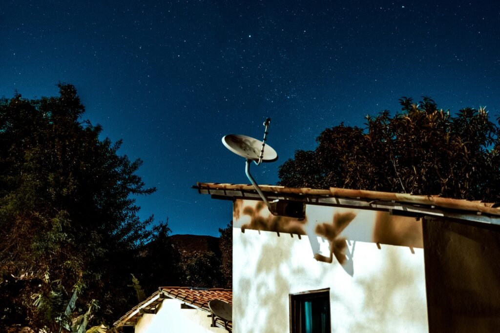 A serene starry night sky over a rural house with a satellite dish, capturing the essence of calm and technology.