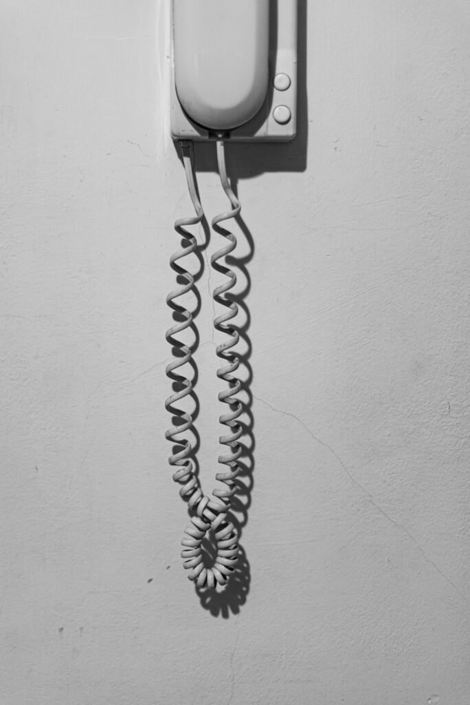 Black and white photo of a vintage wall-mounted telephone with a curly cord.